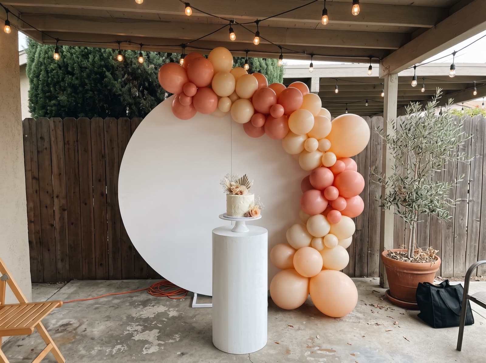 Round balloon backdrop with a peach, coral and cream organic garland and a cake stand at a birthday party